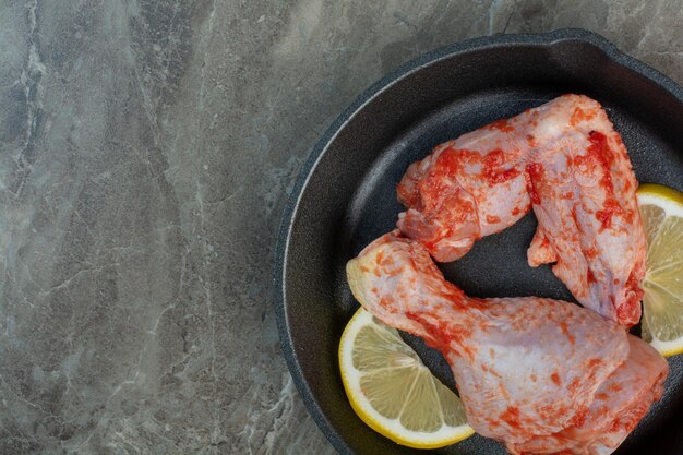 Carne di pollo cruda con spezie e limone in padella scura. Foto di alta qualità