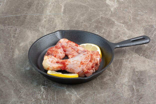 Carne di pollo cruda con spezie e limone in padella scura. Foto di alta qualità