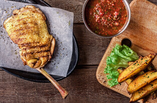 Carne di pollo fritto sull'osso, spicchi di patate, lattuga