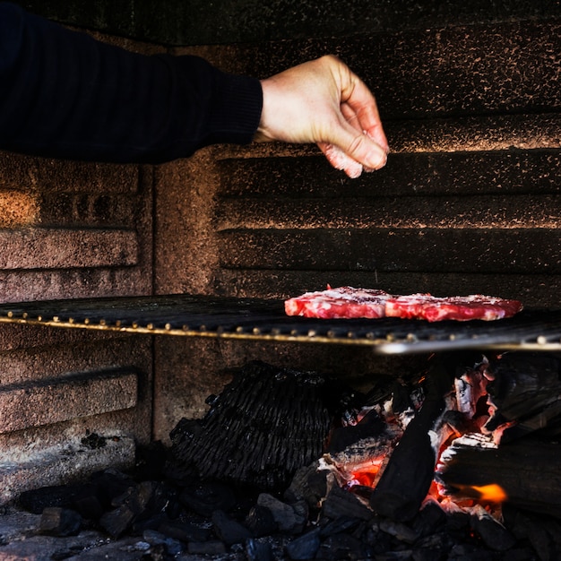 Carne umana condimento a mano sulla griglia del barbecue