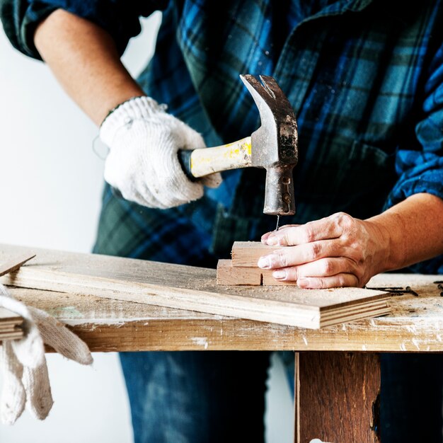 Carpentiere della donna che usando martello che spinge chiodo su un legno