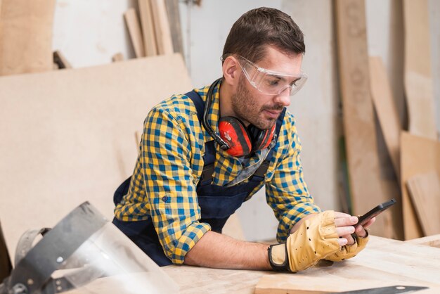 Carpentiere maschio che indossa guanti protettivi guardando smartphone