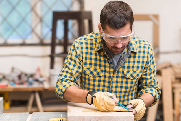 Carpentiere maschio che prende misura con il righello sul blocco di legno