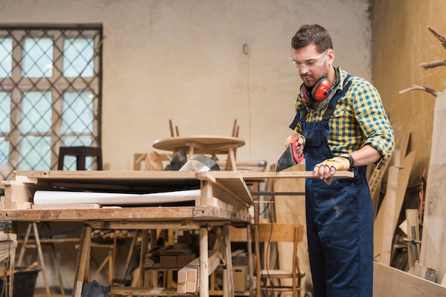 Carpentiere professionista che taglia la plancia di legno con la sega a mano nell&#39;officina