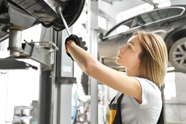 Carrello dell'automobile della riparazione della giovane donna nell'autoservice.