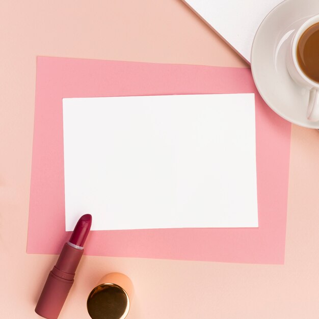 Carta bianca e rosa vuota con rossetto, pennello per trucco e tazza di caffè