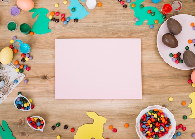 Carta bianca vuota circondata con cioccolatini; coniglietto di Pasqua e caramelle gemme sulla scrivania