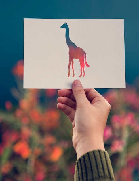 Carta della giraffa della tenuta della mano che scolpisce con il fondo del fiore