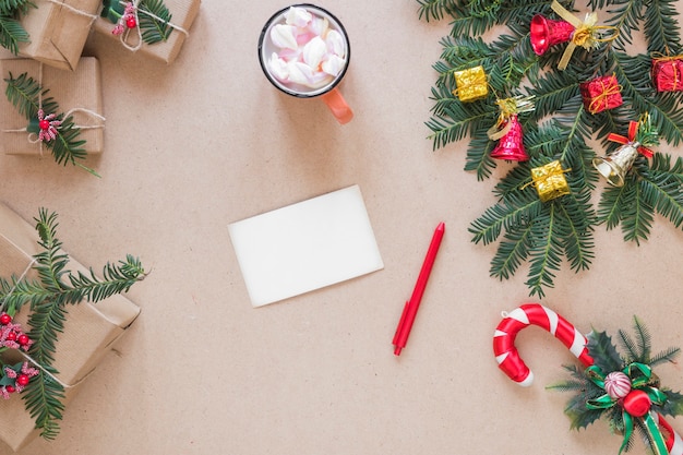 Carta vicino a penna, scatole presenti, ramoscello e tazza di Natale