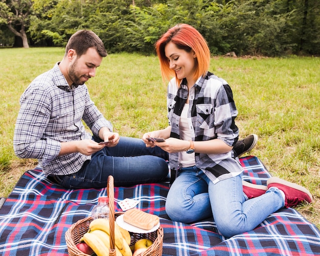 Carte da gioco sorridenti delle giovani coppie sul picnic nel parco