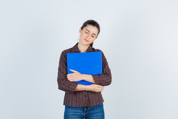 Cartella della tenuta della giovane signora, occhi chiusi in camicia, jeans e vista stanca e frontale.