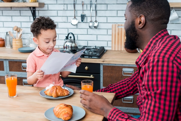 Cartolina d&#39;auguri nera della lettura del figlio mentre facendo colazione con il padre