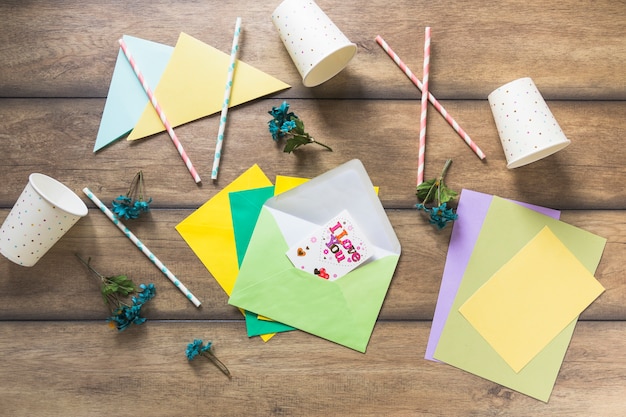 Cartolina d&#39;auguri sulla busta con paglia e tazza monouso sul tavolo di legno