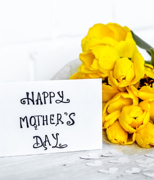 Cartolina festa della mamma e tulipani gialli su uno sfondo di legno chiaro, concetto di vacanza