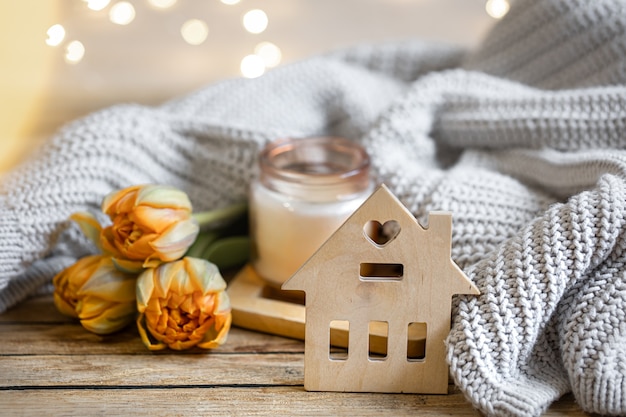 Casa romantica natura morta con candela, decorazioni, fiori e elemento lavorato a maglia su sfondo sfocato con bokeh.