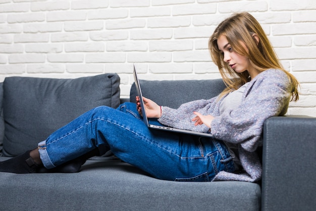 Casa, tecnologia e concetto di internet - occupato ragazza adolescente sdraiato sul divano con il computer portatile a casa