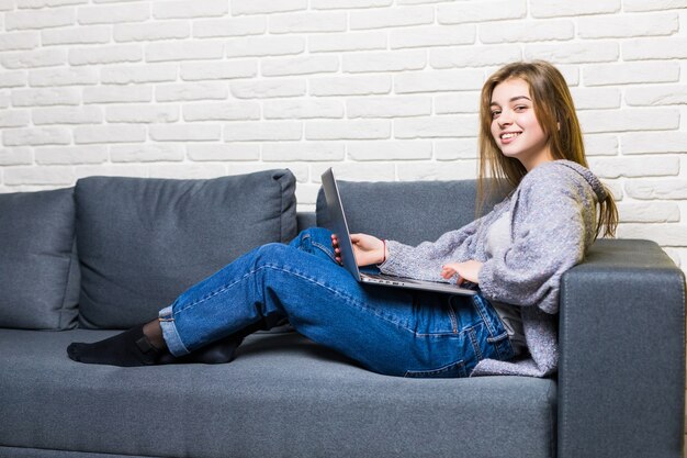 Casa, tecnologia e concetto di internet - occupato ragazza adolescente sdraiato sul divano con il computer portatile a casa