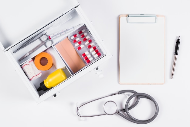 Cassetta di pronto soccorso con appunti; stetoscopio e penna su sfondo bianco