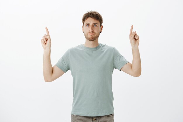 Casual bell'aspetto collega di sesso maschile in maglietta, alzando il dito indice e rivolto verso l'alto mentre fa una smorfia infastidita indifferente