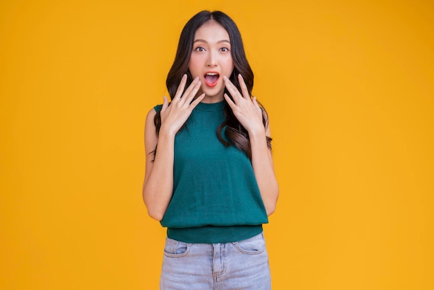 Casual felicità donna asiatica sorridente allegro in maglietta verde blue jean rilassarsi pacifico pensiero positivo spensierato stile di vita in piedi gesto della mano faccia espressione con sfondo di colore giallo