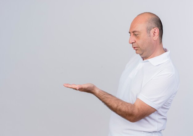 Casual uomo d'affari maturo in piedi in vista di profilo che mostra la mano vuota e guardando isolato su sfondo bianco con copia spazio