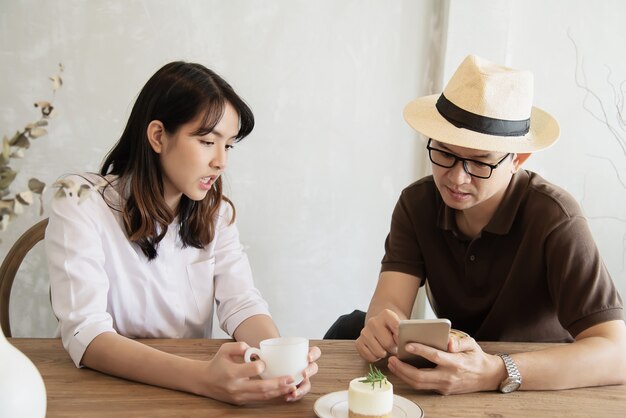 Casual uomo e donna parlando felicemente mentre bere un caffè e guardando il telefono cellulare