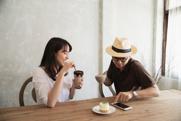 Casual uomo e donna parlando felicemente mentre bere un caffè e guardando il telefono cellulare