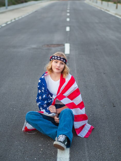 Caucasica patriottica seduta in mezzo alla strada con la bandiera degli Stati Uniti drappeggiata intorno a lei