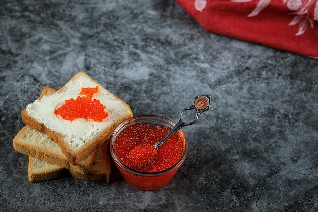 Caviale rosso in un barattolo di vetro e su fette di pane