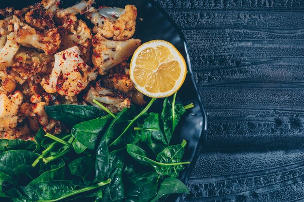 Cavolfiore fritto vista dall'alto nel piatto con verdure e limone su fondo di legno scuro. orizzontale