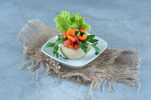Cavolfiore sotto foglie di prezzemolo, lattuga e verdure tritate su un piatto su un tavolo di marmo.