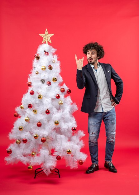 celebrazione di natale con il giovane emozionante divertente felice che fa gesto di vittoria e che sta vicino all'albero di Natale