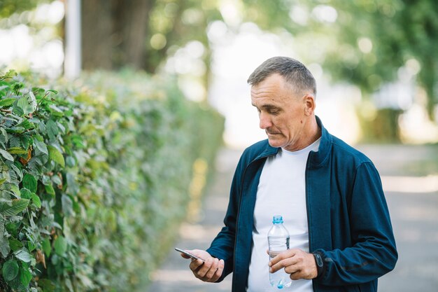 Cellulare di sguardo all'aperto dell'uomo senior