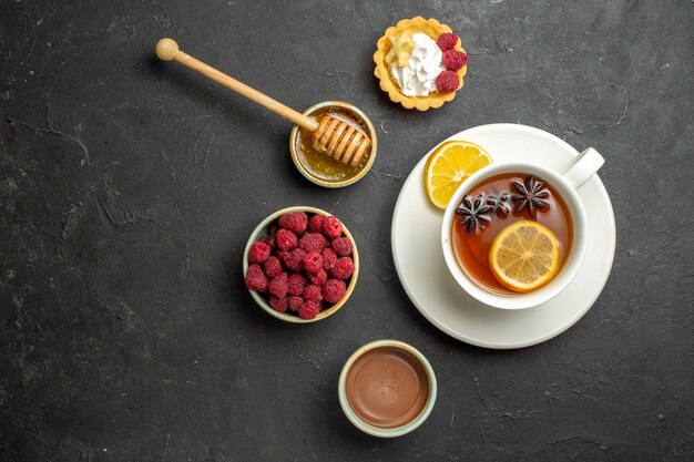 Cena gustosa con una tazza di tè nero con biscotti al miele di lampone e cioccolato al limone su sfondo scuro