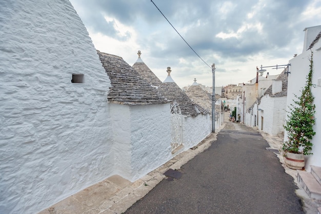 Centro storico vuoto di Alberobello con case Trulli tra piante verdi e fiori, principale distretto turistico, Puglia, Italia meridionale. Tipiche costruzioni costruite con muretti a secco e tetto conico