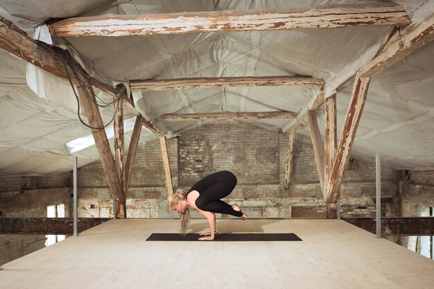 Cercando. Una giovane donna atletica esercita lo yoga su un edificio abbandonato. Equilibrio della salute mentale e fisica. Concetto di stile di vita sano, sport, attività, perdita di peso, concentrazione.