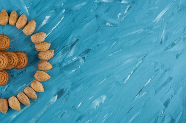 Cerchio di mandorle in guscio con biscotti dolci freschi rotondi su sfondo blu.