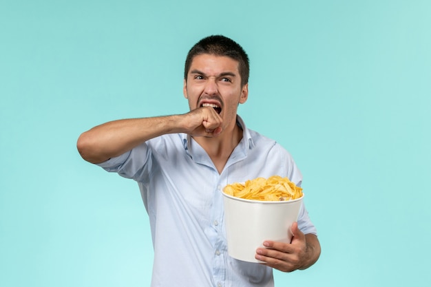 Cestino della holding del giovane di vista frontale con le patatine fritte su un cinema maschio remoto solitario della parete blu