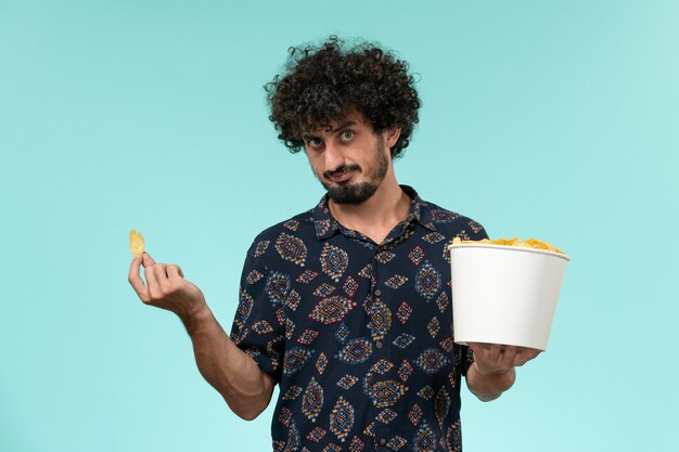 Cestino della holding del giovane di vista frontale con le patatine fritte su un film maschio remoto del cinema della pellicola della parete blu