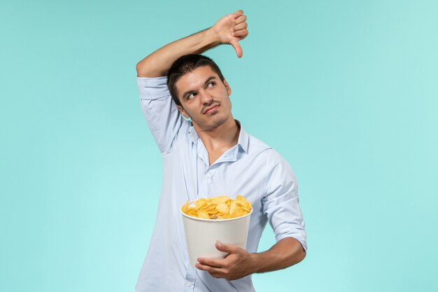 Cestino della holding del giovane di vista frontale con le patatine fritte su un maschio solitario del cinema remoto della parete blu