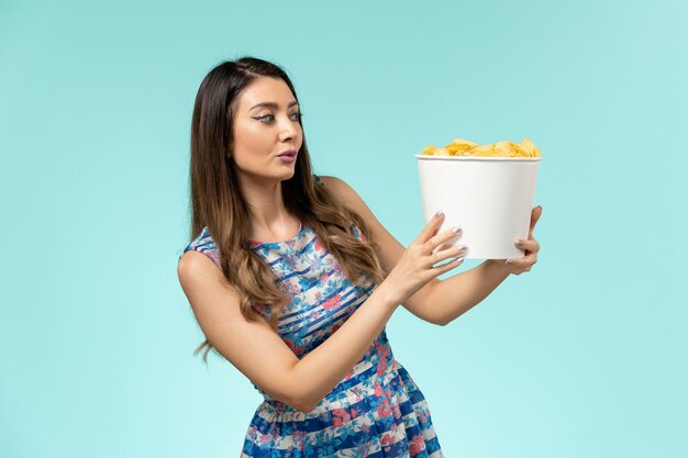 Cestino della holding della giovane femmina di vista frontale con patatine fritte e guardare film sulla superficie blu-chiaro