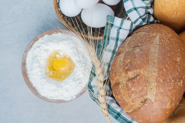 Cestino di pane vario insieme a farina e uova. Foto di alta qualità