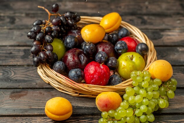 Cestino di vista frontale con frutta dolce e aspro come prugne albicocche uva sullo scrittorio rustico marrone