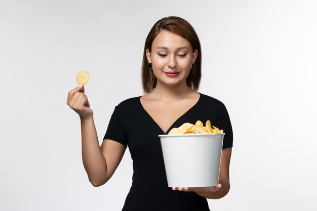 Cestino femminile giovane della tenuta di vista frontale con le patatine fritte sulla superficie bianca