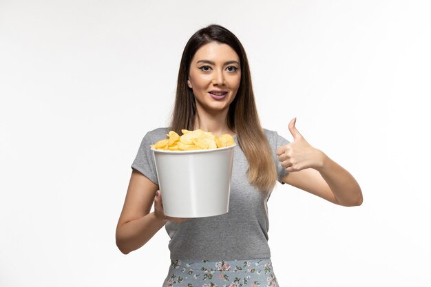 Cestino femminile giovane della tenuta di vista frontale con le patatine fritte sulla superficie bianca