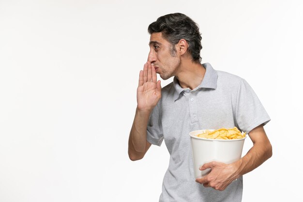 Cestino maschio giovane della tenuta di vista frontale con le patatine fritte e parlando con qualcuno sulla superficie bianca