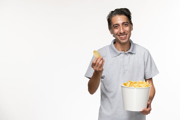 Cestino maschio giovane della tenuta di vista frontale con le patatine fritte sulla superficie bianca chiara