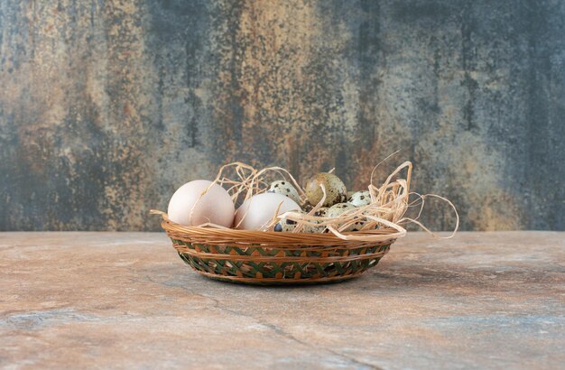 Cesto di vimini pieno con uova di quaglia su marmo