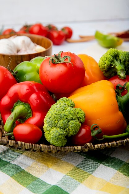 Cesto pieno di verdure come pomodori, peperoni e scalogno su tela a scacchi