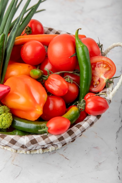 Cesto pieno di verdure come pomodori, peperoni e scalogno sulla superficie bianca